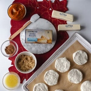 Overhead photo of biscuit dough rounds, melted butter, brown sugar, and pumpkin pie filling arranged on a baking tray.