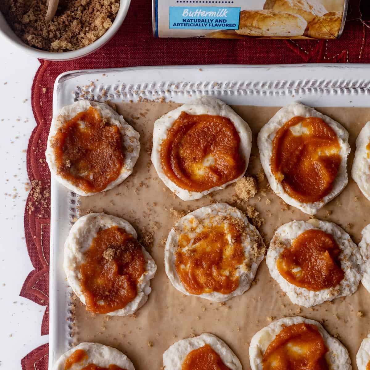 Biscuit rounds spread with pumpkin filling and sprinkled with brown sugar, ready to bake into pumpkin pull apart bread.