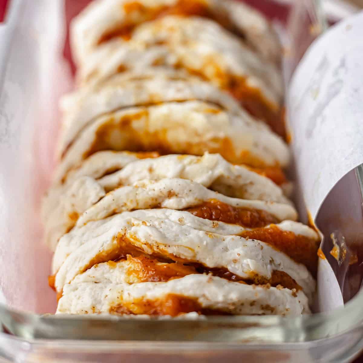 Stacked biscuit dough rounds filled with pumpkin pie filling and brown sugar, arranged vertically in a loaf pan.
