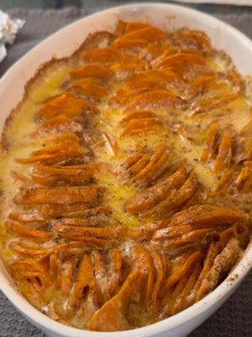 scalloped sweet potatoes in a white casserole dish